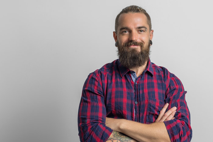 middle aged man wearing a plaid shirt with facial piercings and a beard