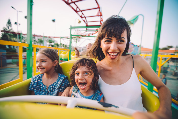 young, dark-haired woman with bangs on a small roller coaster with 2 children